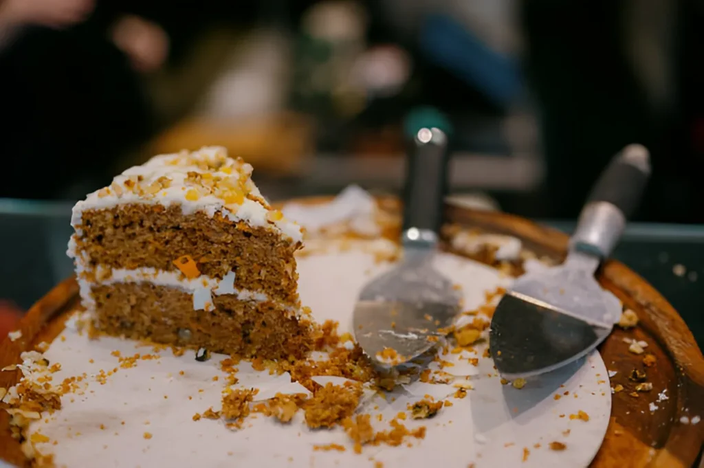 A beautifully frosted carrot cake topped with candied carrots and chopped walnuts on a rustic wooden table.