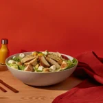 Hearty Caesar salad dinner with grilled chicken, croutons, romaine, Parmesan, avocado, and chickpeas on a rustic plate.