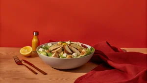 Hearty Caesar salad dinner with grilled chicken, croutons, romaine, Parmesan, avocado, and chickpeas on a rustic plate.
